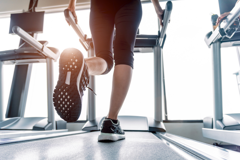 Lower body at legs part of Fitness girl running on running machine or treadmill in fitness gym with sun ray. Warm tone. Healthy and Exercise activity concept. Workout and  Strength training theme.